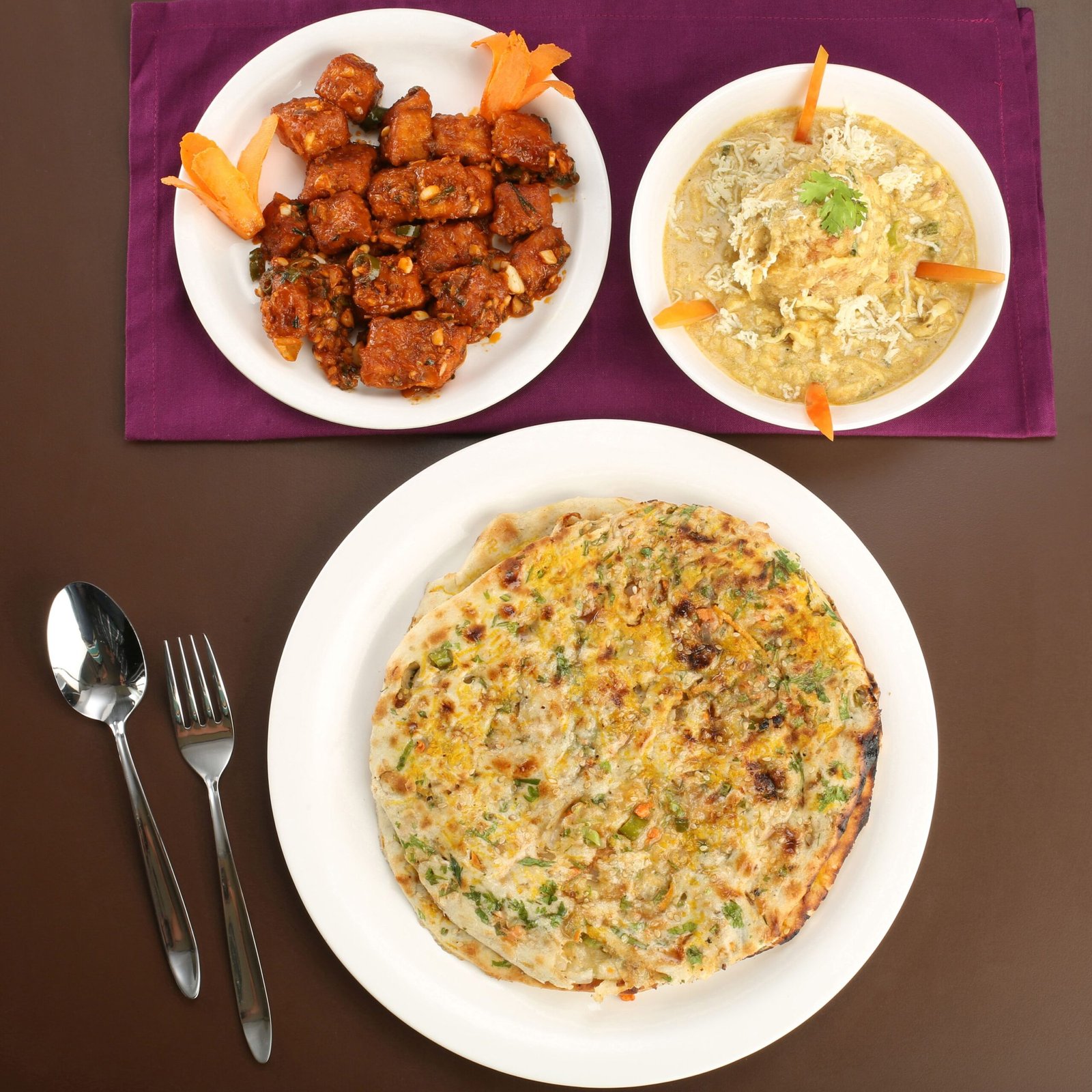 A top view of Indian dishes including an egg omelette, spicy curries, and cutlery on a table.